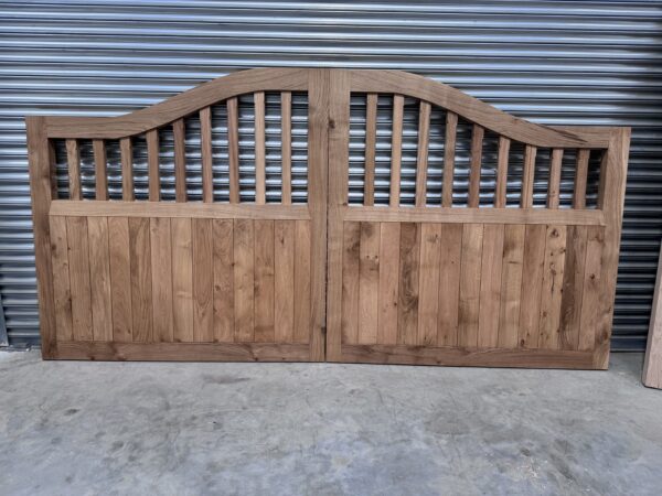 A pair of wooden oak swan neck driveway gates leaning against metal shutter