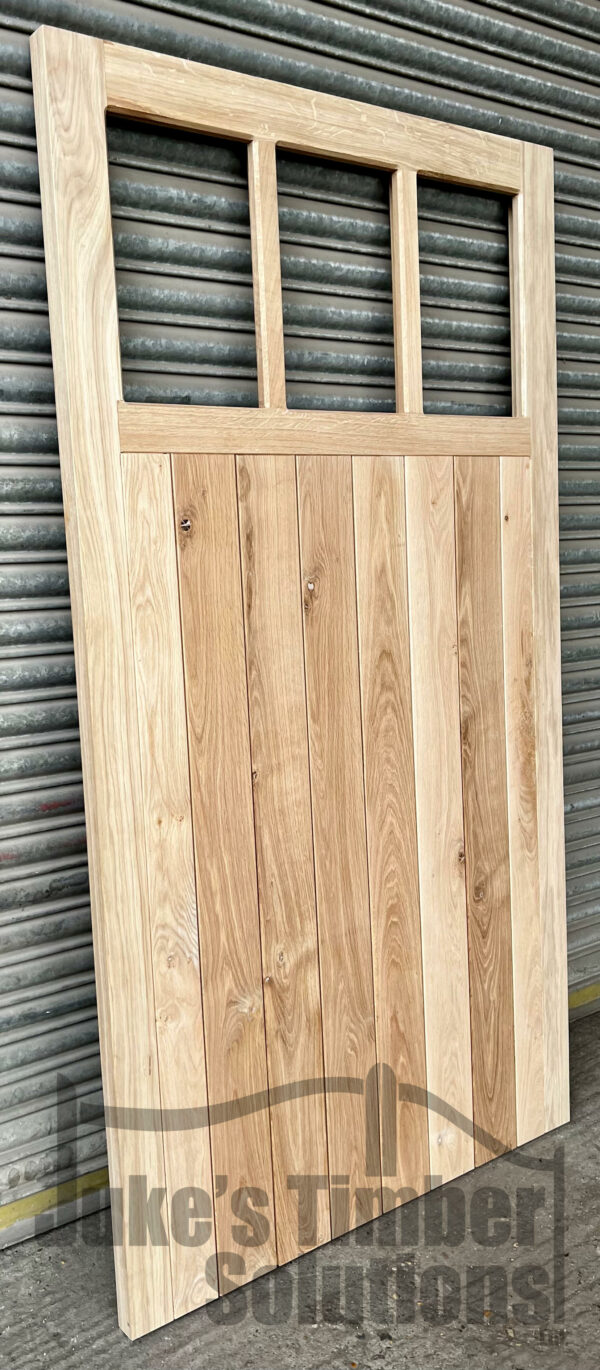 Three pane oak garage side door leaning against metal shutters, pictured outside.