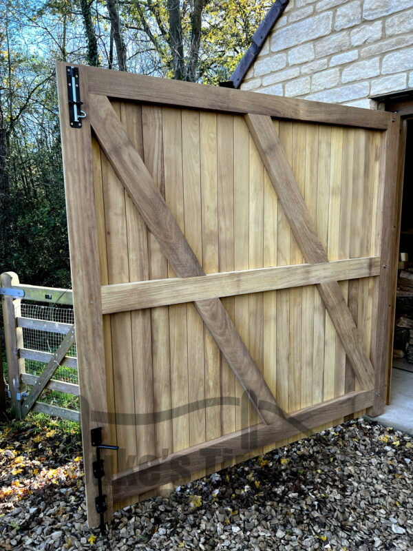 Left hand side of a set of Iroko super heavy duty garage doors, opened to show the interior. Doors are fitted to a stone garage, with a gravel drive.