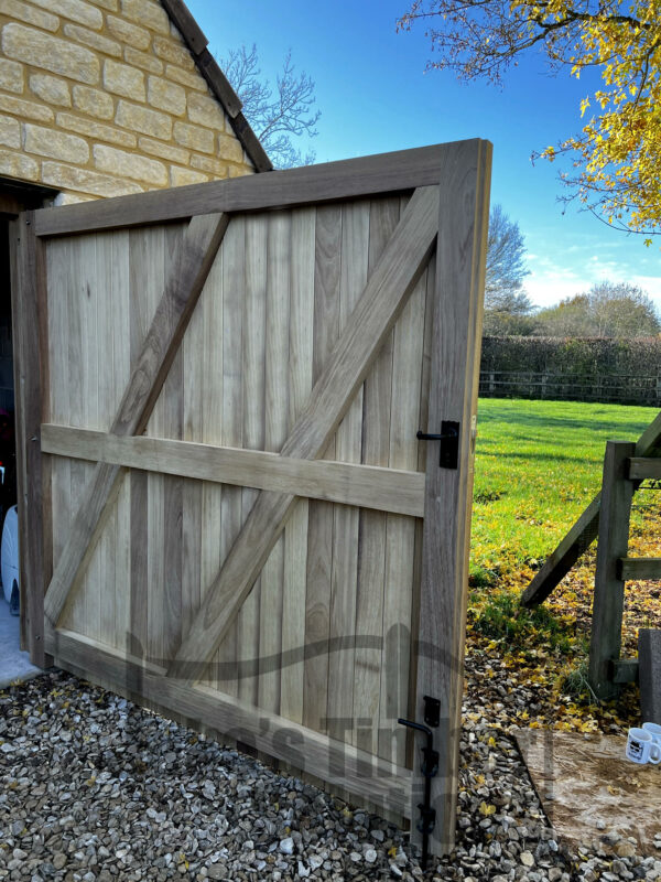 Right hand side of a set of Iroko super heavy duty garage doors, opened to show the interior. Doors are fitted to a stone garage, with a gravel drive.
