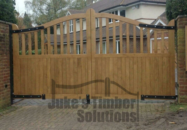 Wooden oak swan neck palisade driveway gates installed onto brick wall at the end of a block driveway