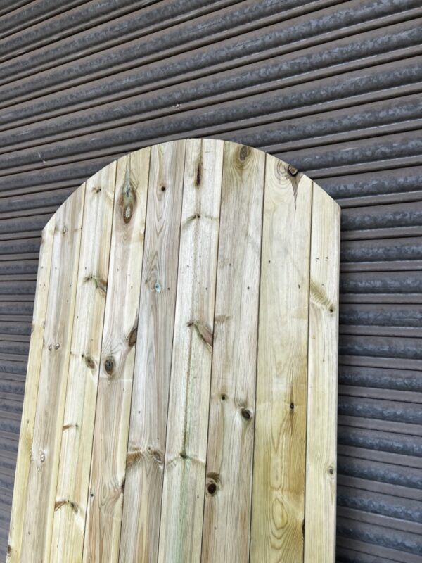 Curved top tanalised matchboard garden gate leaning against metal shutters