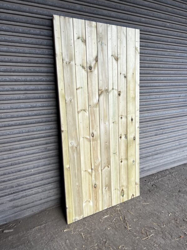 Tanalised matchboard garden gate, leaning against metal shutter