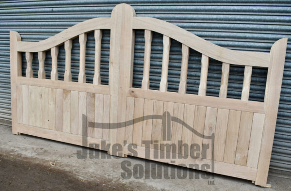 A pair of light oak swan neck driveway gates with spindles, pictured leaning against metal shutter.
